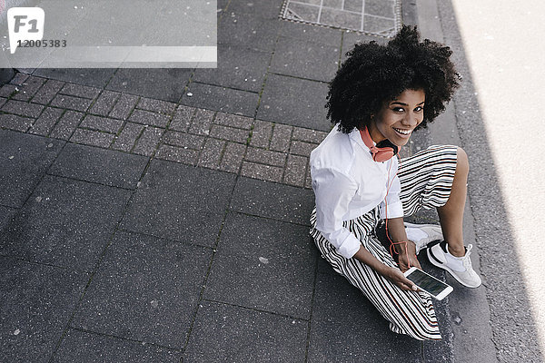 Lächelnde junge Frau auf dem Bürgersteig sitzend