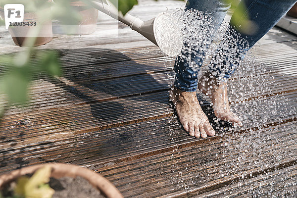 Frau mit Gießkanne  die Wasser über ihre Füße gießt.