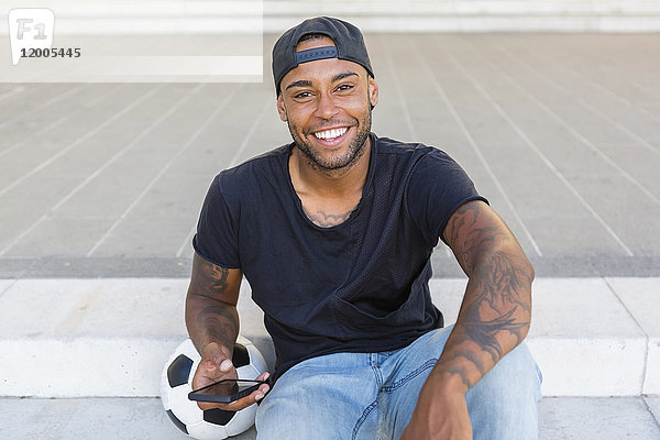 Porträt eines lachenden jungen Mannes mit Smartphone