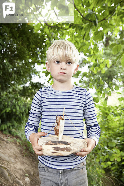 Junge mit geschnitztem Holzboot im Wald