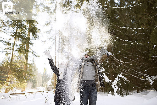 Glückliches junges Paar  das Schnee in die Luft wirft.