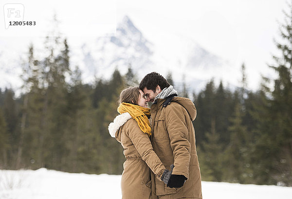 Glückliches junges Paar steht Kopf an Kopf in der Winterlandschaft