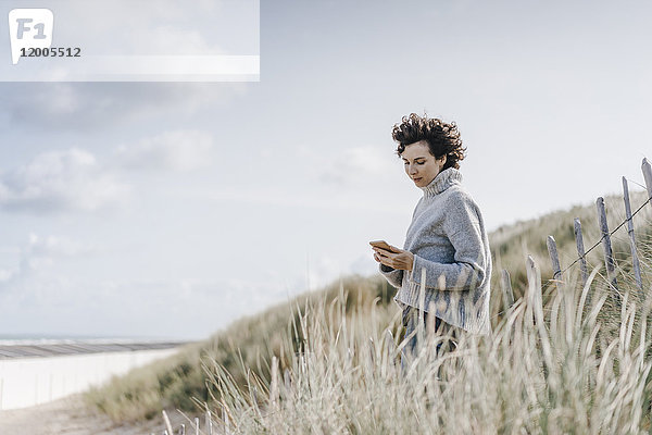 Frau steht in der Stranddüne mit dem Handy