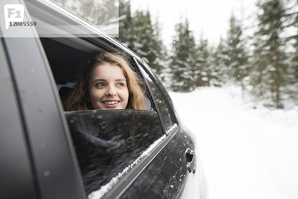 Junge Frau blickt aus dem Autofenster in die Winterlandschaft