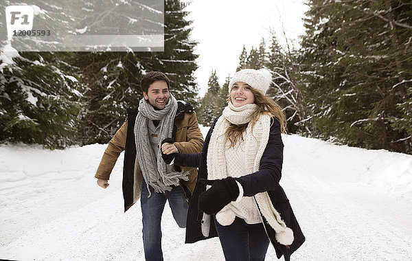 Glückliches junges Paar beim Laufen in verschneiter Winterlandschaft