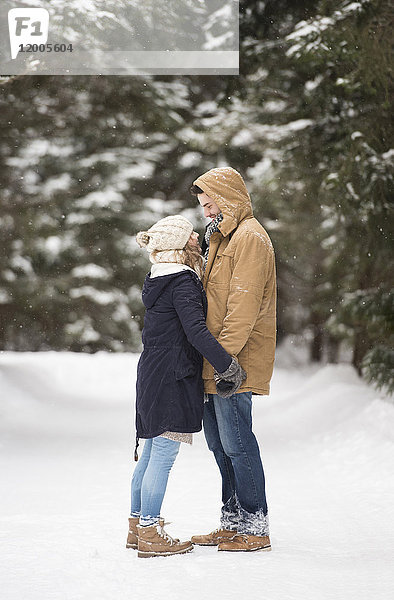 Fröhliches junges Paar steht sich gegenüber in verschneiter Winterlandschaft