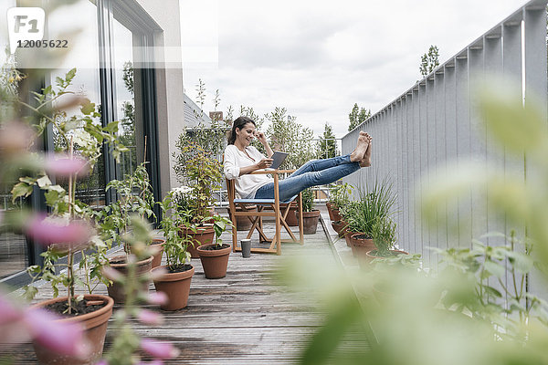 Lächelnde Frau entspannt auf dem Balkon mit Tablette