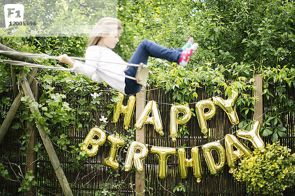 Dekoration für Geburtstagsfeier im Garten mit goldenen Luftballons und schwingendem Mädchen im Vordergrund