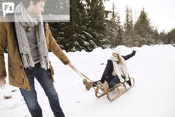 Glückliches junges Paar mit Schlitten im Winterwald