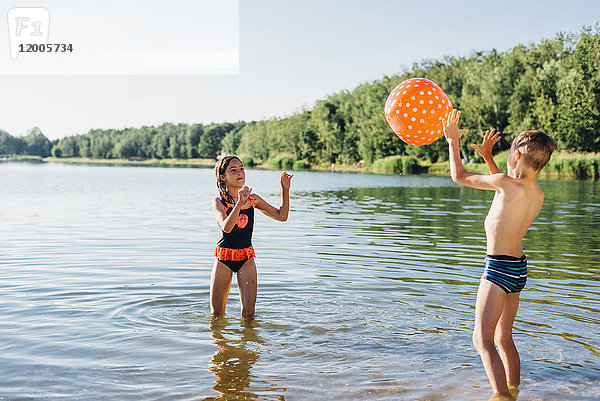 Junge und Mädchen stehen am Seeufer und spielen mit Strandball