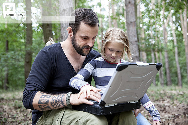 Vater und Tochter im Wald mit Laptop