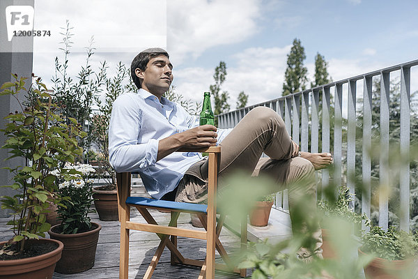 Mann mit Flasche entspannt auf dem Balkon