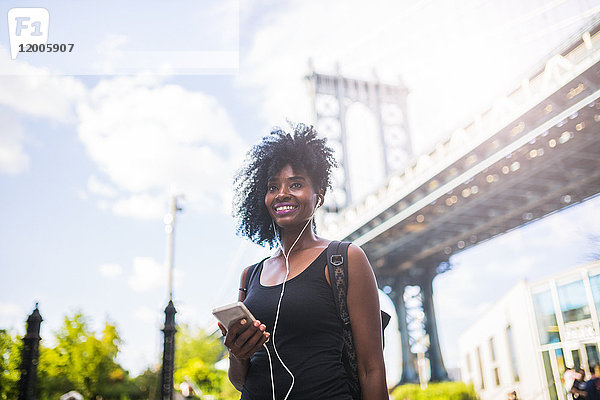 USA  New York City  Brooklyn  lächelnde Frau beim Musikhören an der Manhattan Bridge