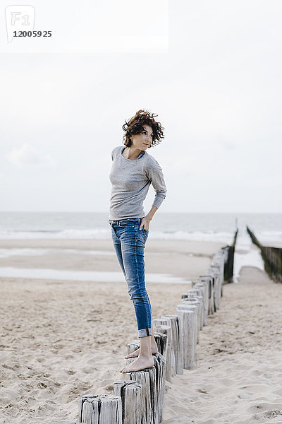 Frau auf Holzpfahl am Strand stehend