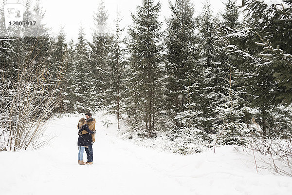 Fröhliches junges Paar im schneebedeckten Winterwald gegenüber stehend
