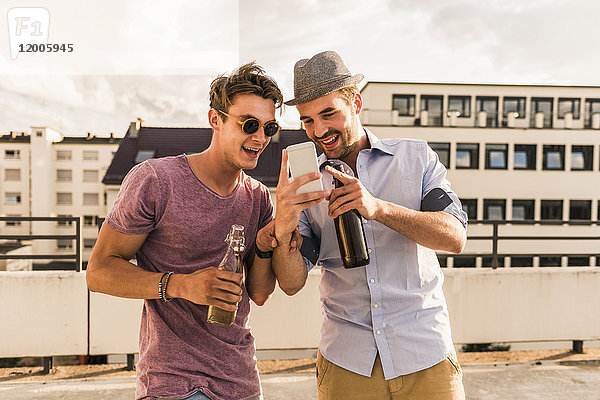 Zwei Freunde mit Bierflaschen und Handy auf dem Dach