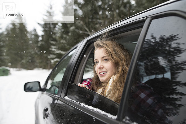 Junge Frau blickt aus dem Autofenster in die Winterlandschaft