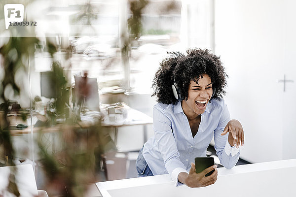 Fröhliche junge Frau beim Musikhören im Büro
