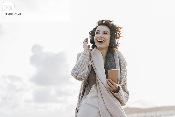 Glückliche Frau am Strand mit Handy und Kopfhörer