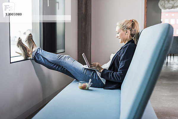 Lächelnde Geschäftsfrau auf der Couch sitzend mit den Füßen nach oben mit Tablette