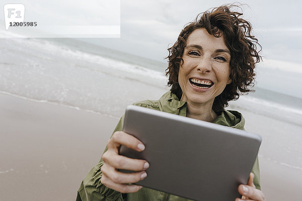 Porträt einer glücklichen Frau mit Tablette am Strand