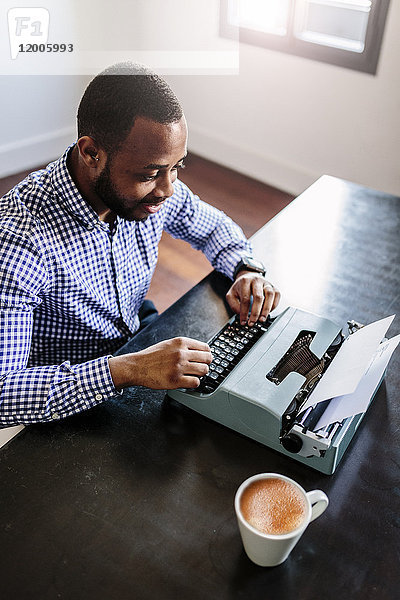 Junger Mann am Schreibtisch mit Schreibmaschine