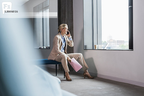 Lächelnde Geschäftsfrau am Telefon sitzend am Fenster