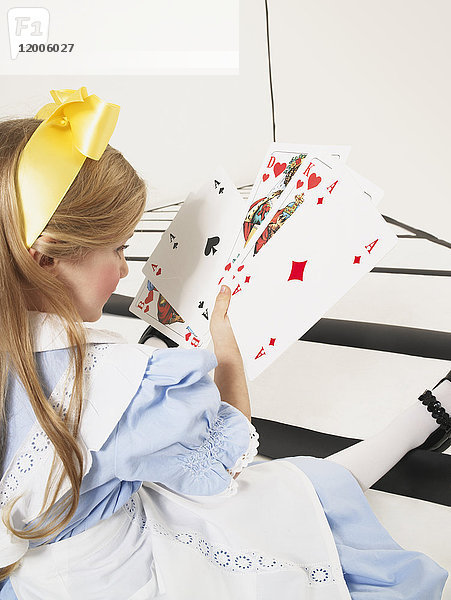 Kleines Mädchen verkleidet als Alice im Wunderland mit übergroßen Spielkarten