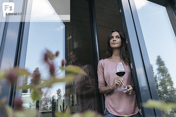 Frau hält ein Glas Rotwein und schaut aus dem Fenster.