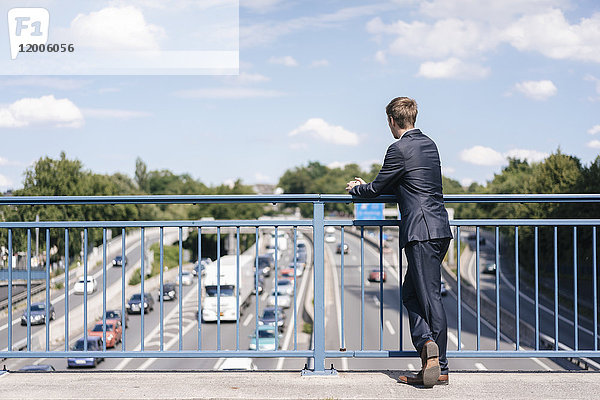 Geschäftsmann steht auf einer Brücke über eine Autobahn