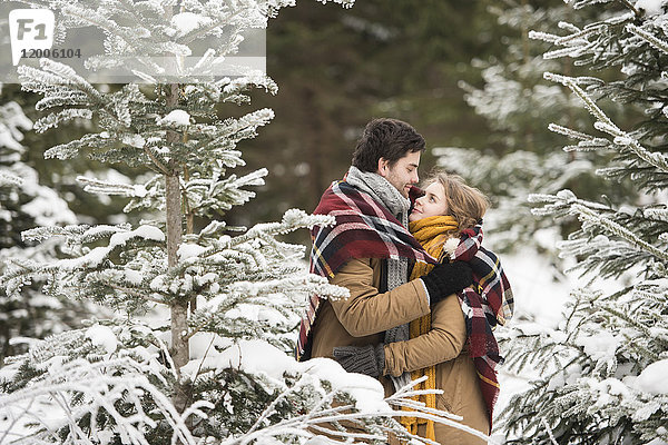 Glückliches junges Paar in Decke gehüllt im Winterwald stehend