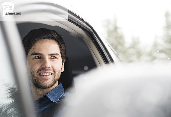 Porträt eines lächelnden jungen Mannes beim Autofahren im Winter
