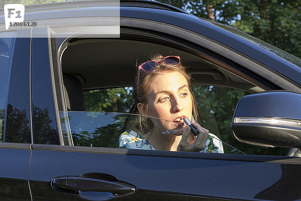Junge Frau im Auto sitzend  Lippenstift auftragend