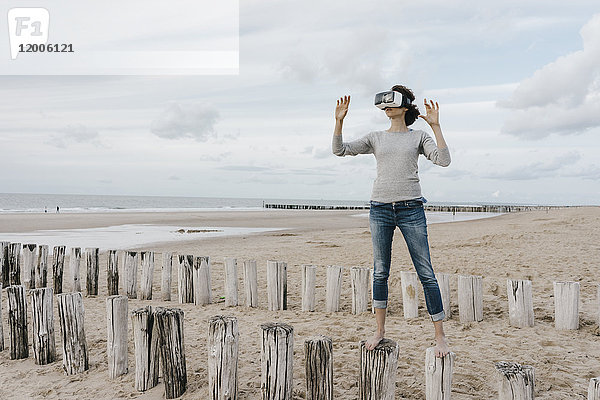 Frau auf Holzpfählen am Strand stehend mit VR-Brille