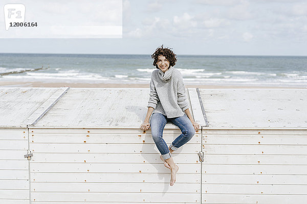Lächelnde Frau auf Holzkiste am Strand sitzend
