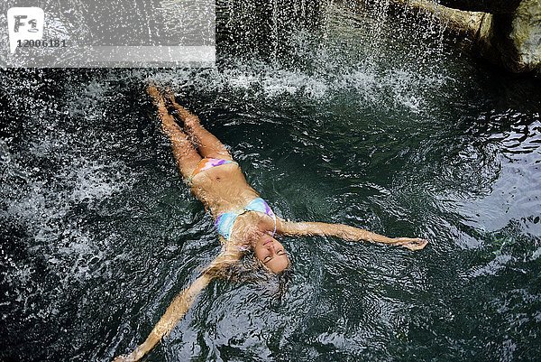 Junge Frau im Wasser schwimmend im Pool mit Wasserfall