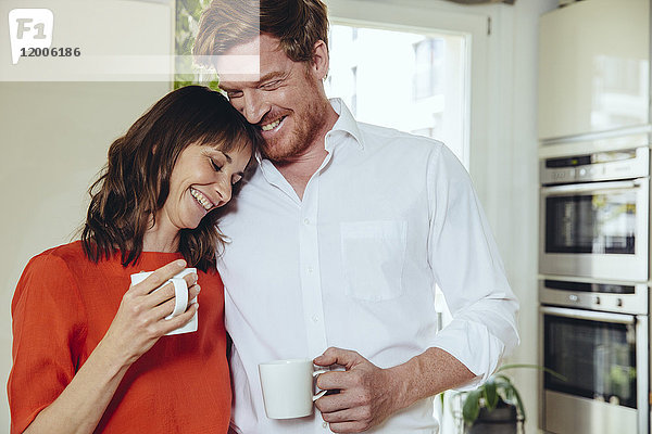 Glückliches Paar in der Küche mit Kaffeebechern