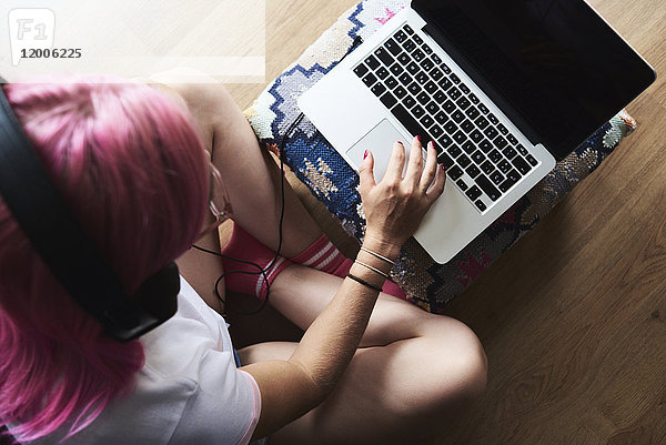 Junge Frau mit rosa Haaren  die Kopfhörer trägt und den Laptop zu Hause benutzt.