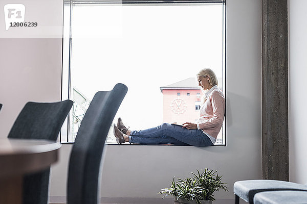 Geschäftsfrau auf der Fensterbank sitzend mit Tablette