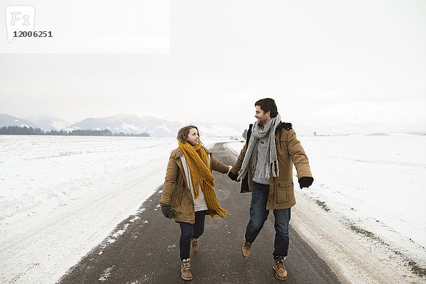 Verliebtes junges Paar geht auf leerer Landstraße in verschneiter Landschaft spazieren