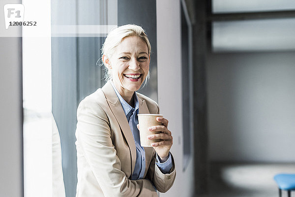 Porträt einer glücklichen Geschäftsfrau mit Kaffee am Fenster