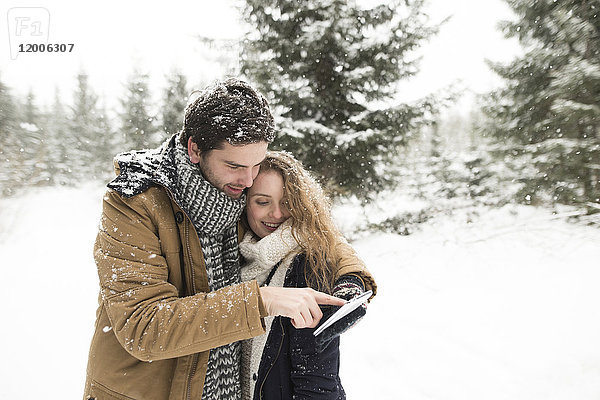 Glückliches junges Paar steht mit dem Handy im verschneiten Winterwald