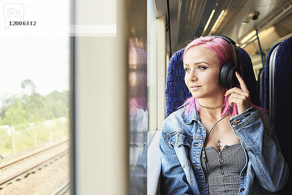 Junge Frau mit rosa Haaren hört Musik während einer Zugfahrt