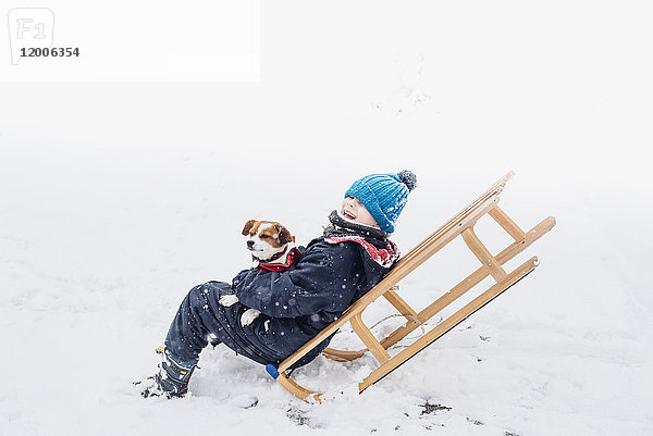 Kleiner Junge mit seinem Hund auf einem Schlitten im Schnee