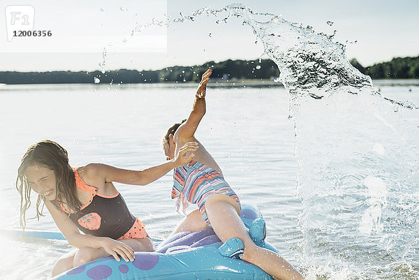 Zwei Mädchen sitzen auf einem Schwimmspielzeug im Wasser.