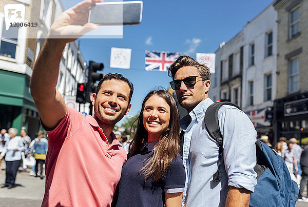 UK  London  Portobello Road  Porträt von drei Freunden  die Selfie mit dem Smartphone nehmen.