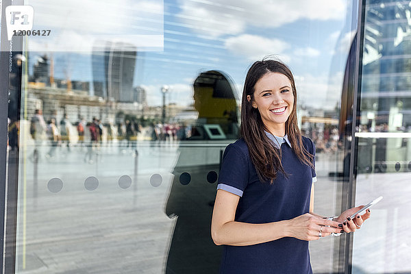 UK  London  Portrait einer lächelnden Frau mit Smartphone in der Stadt