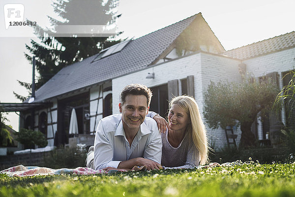 Ein glückliches Paar liegt auf Gras im Garten ihres Landhauses.