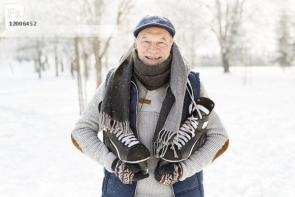 Lächelnder Senior mit Schlittschuhen im Winterwald