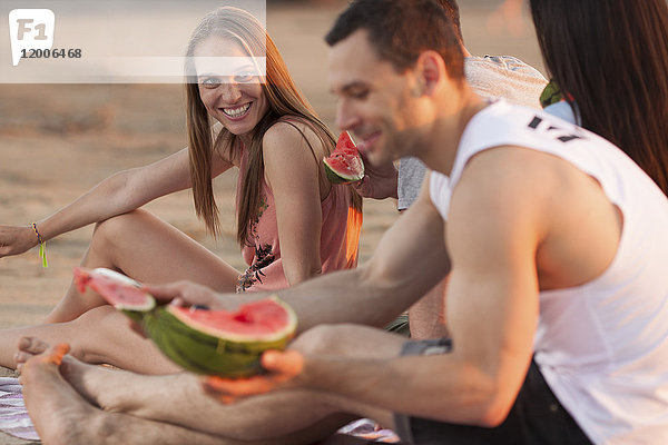 Glückliches Paar mit Freunden am Strand beim Essen von Wassermelone